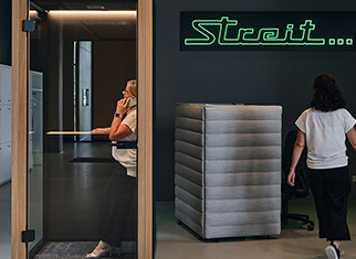 Multispace Büro - Das Allroundtalent für Modernes Arbeiten Mitarbeiterin von Streit Service & Solution telefoniert in einem Multispace Büro. Eine weitere Mitarbeiterin von Streit Service & Solution läuft daran vorbei. Im Hintergrund hängt ein Neon-Sign mit grüner Schrift und dem Satz Streit... in allen Büros.