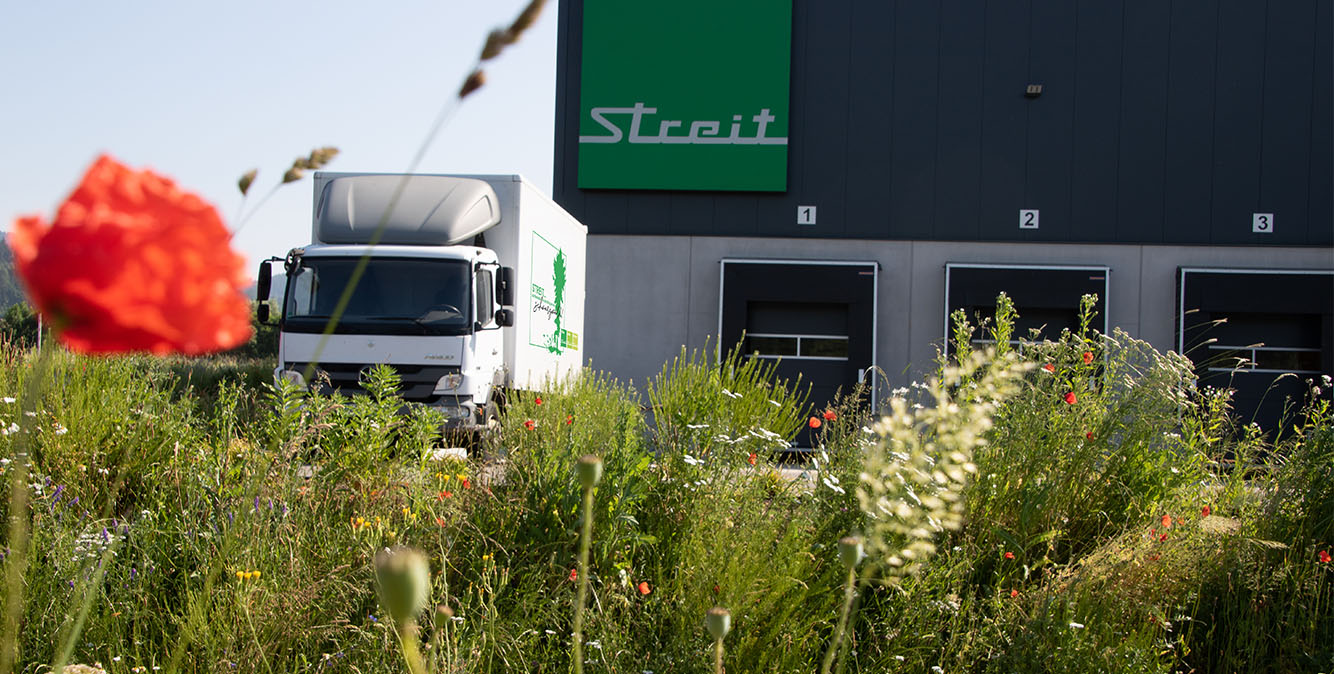 Nachhaltigkeit bei STREIT Eine Wiese Mit Blumen. Im Hintergrund steht ein LKW vor dem Logistikzentrum von STREIT