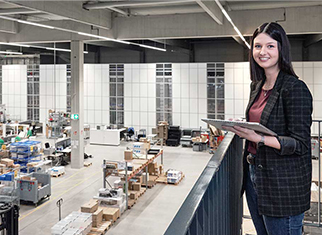 Effiziente Kommissionierung durch moderne Autostore-Anlage von STREIT  Mitarbeiterin von Streit Service & Solution steht im modernen Logistikzentrum und arbeitet an einem Tablet. Im Hintergrund ist die Autostore Anlage zu sehen.